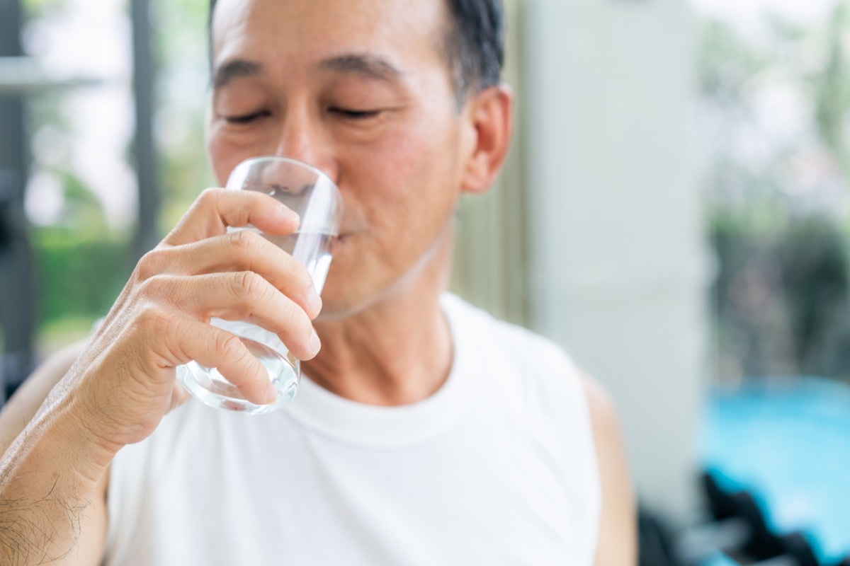 Senior man drink mineral water in gym fitness center after exercise. Elderly healthy lifestyle.