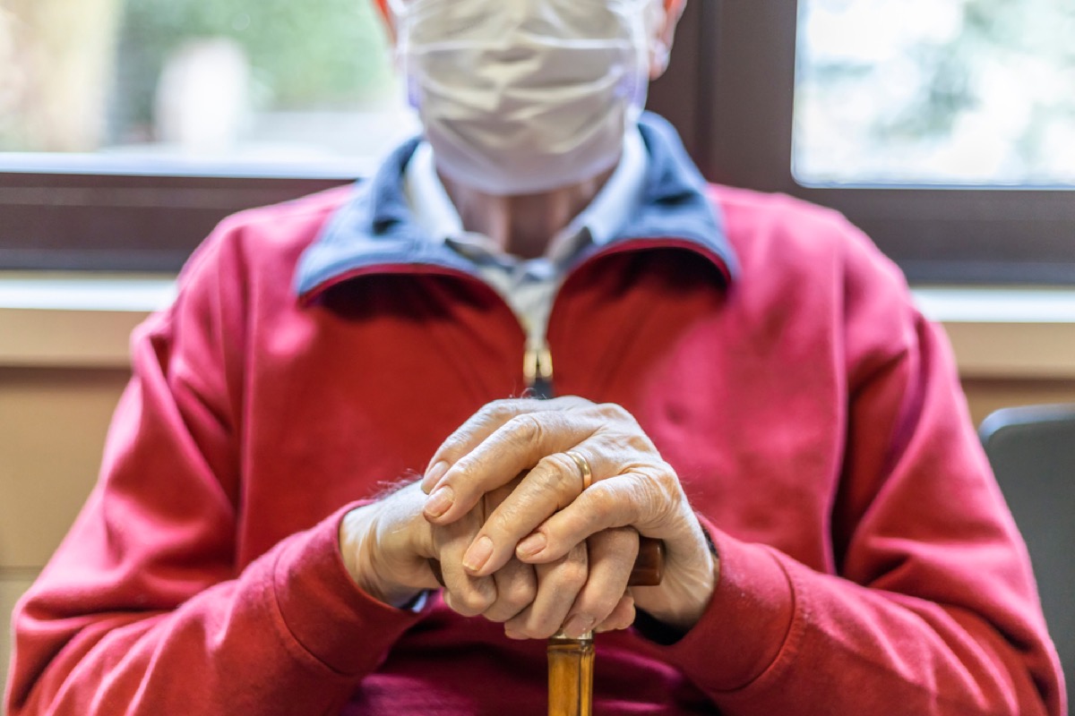 closeup of man in mask sitting in doctor's waiting room with cane