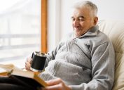 Senior man old sitting and Reading a book at the retirement nursing home with cup of tea in hand