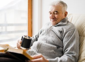 Senior man old sitting and Reading a book at the retirement nursing home with cup of tea in hand
