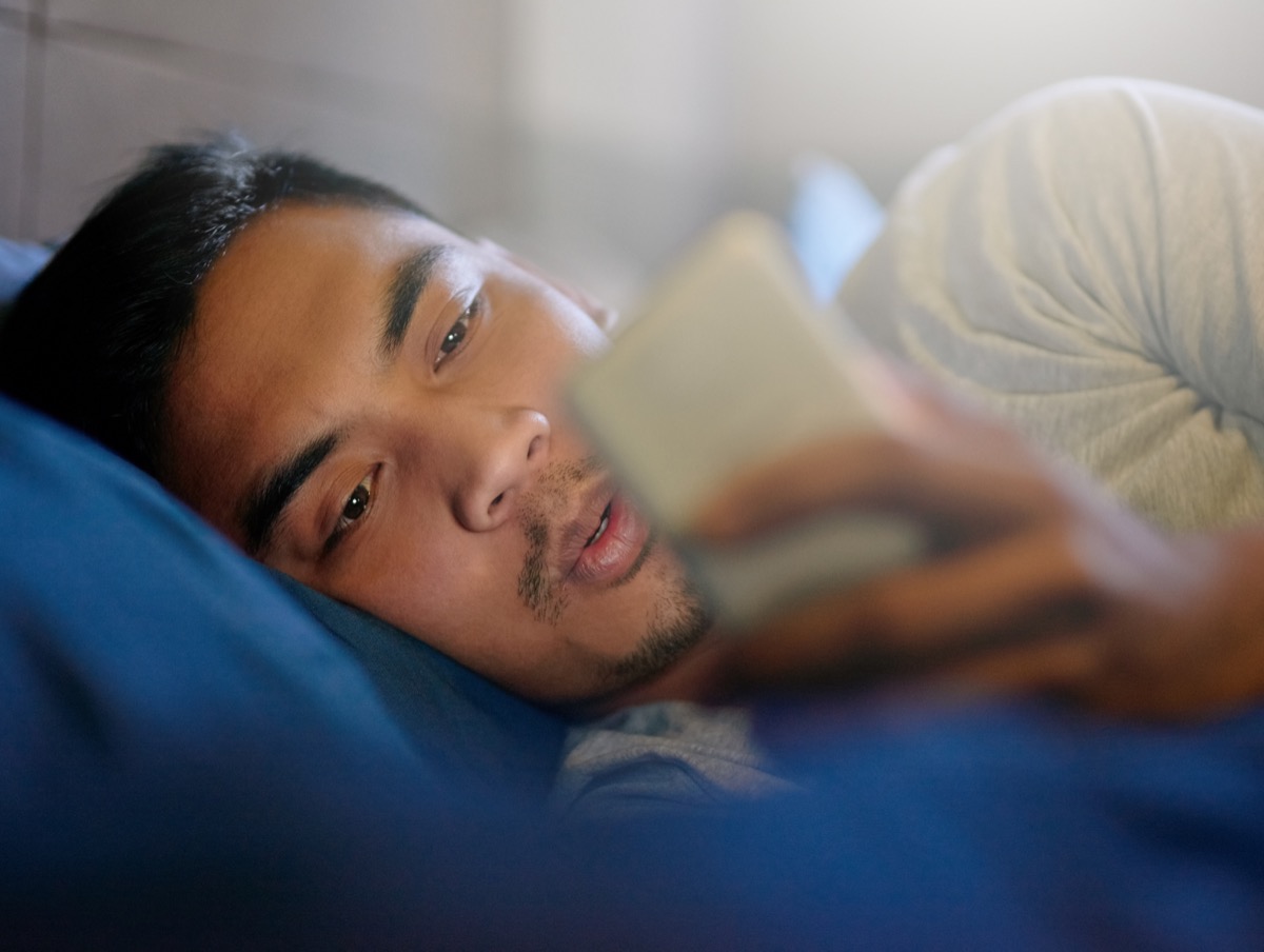 Shot of a young man looking at his phone while lying in bed