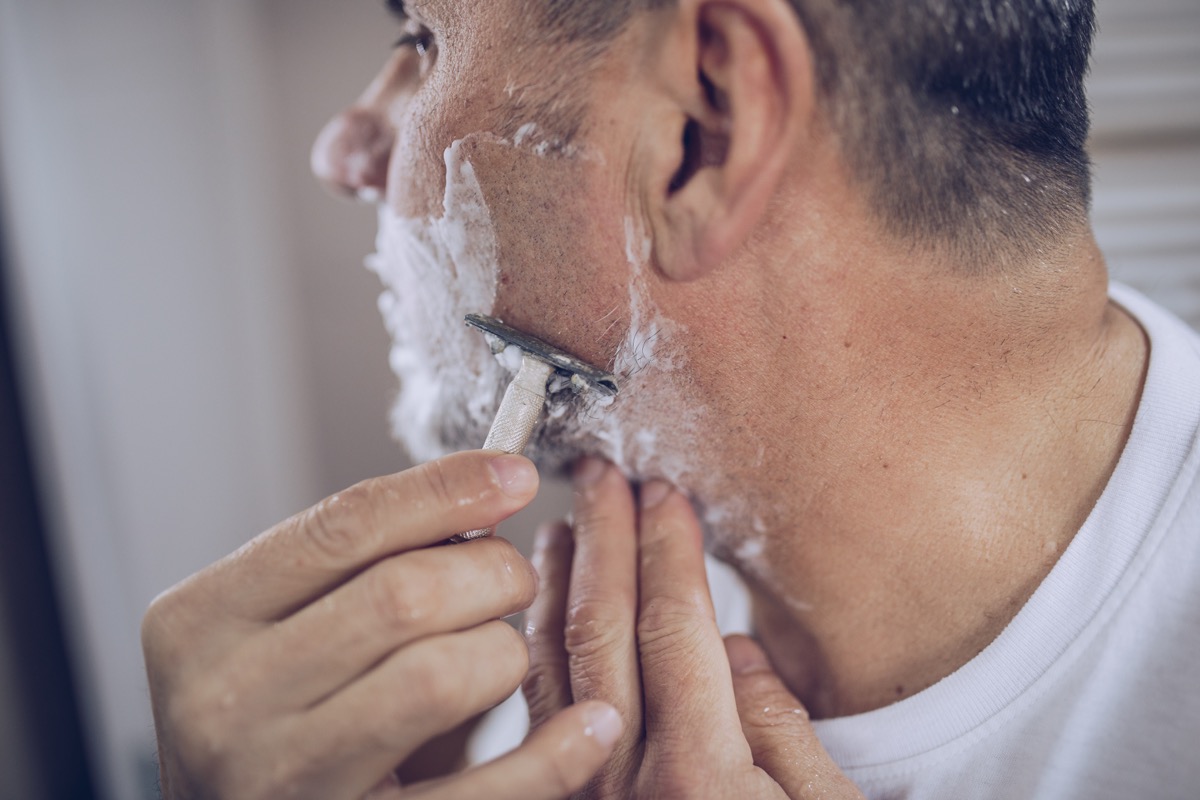 An older man shaves, preparing for work