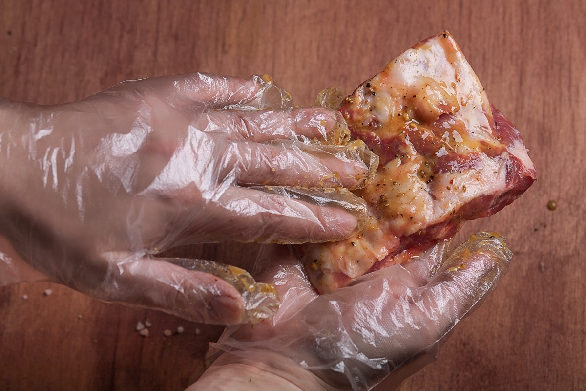 gloved hands marinating a piece of meat