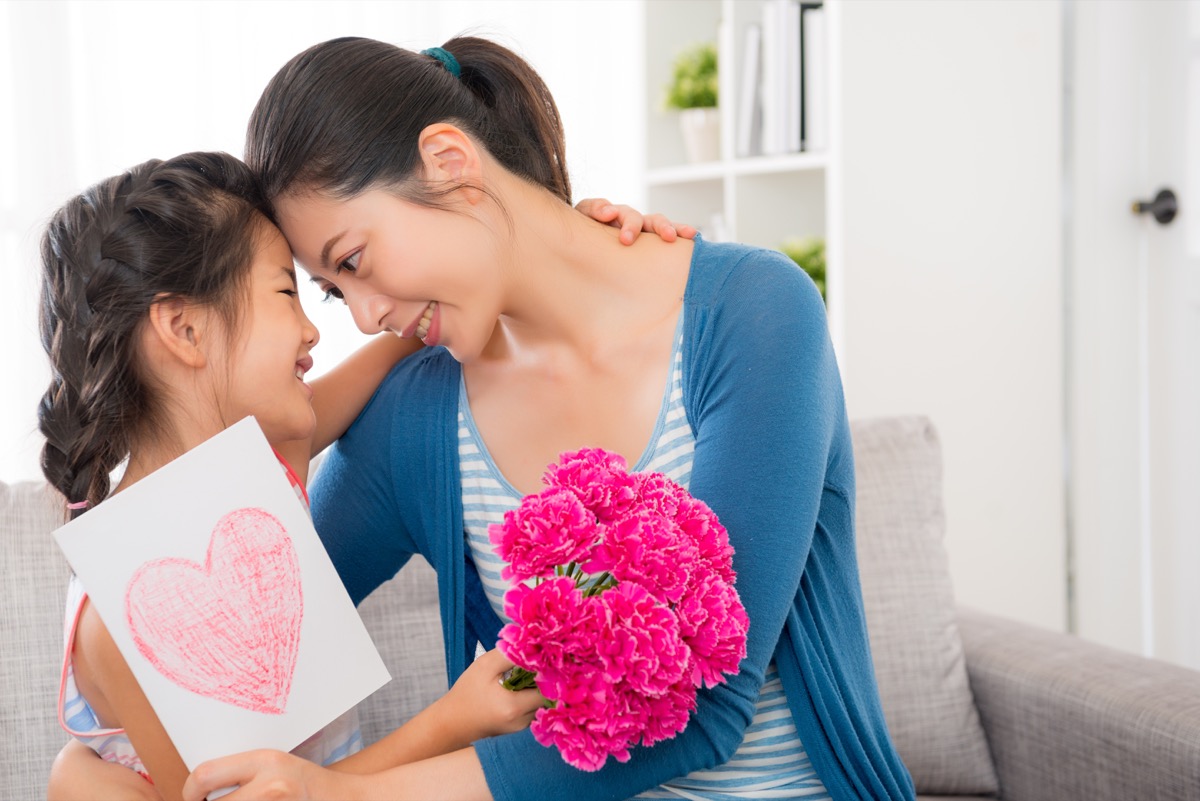 Young girl holding flowers and hugging her mom, who is holding a card. 