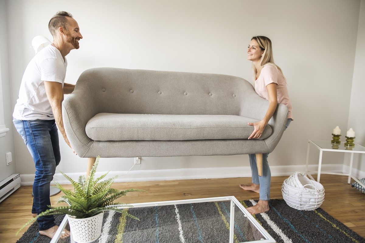 A Full length of happy couple placing sofa in living room of new home