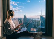 girl sits on windowsill overlooking nyc skyline