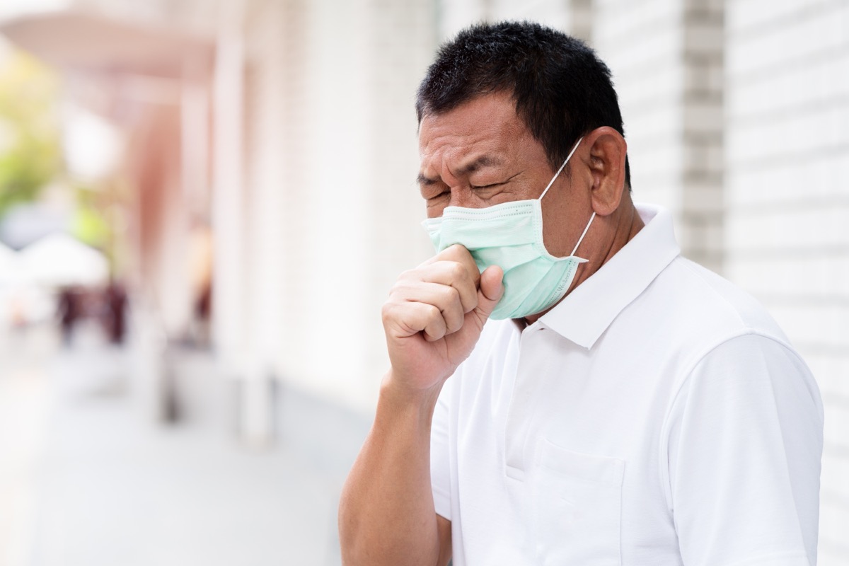 older asian man wearing face mask and coughing