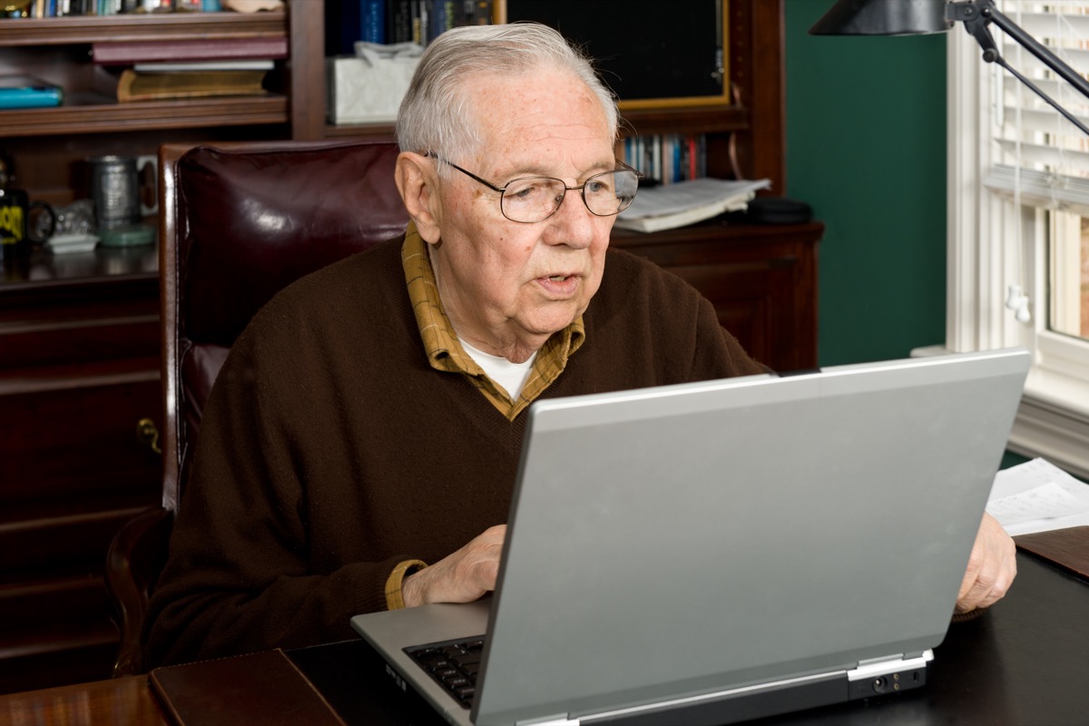 older white man looking at laptop in home office