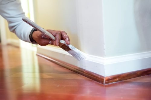 Painter is using a paint brush to paint baseboard in a home. RM