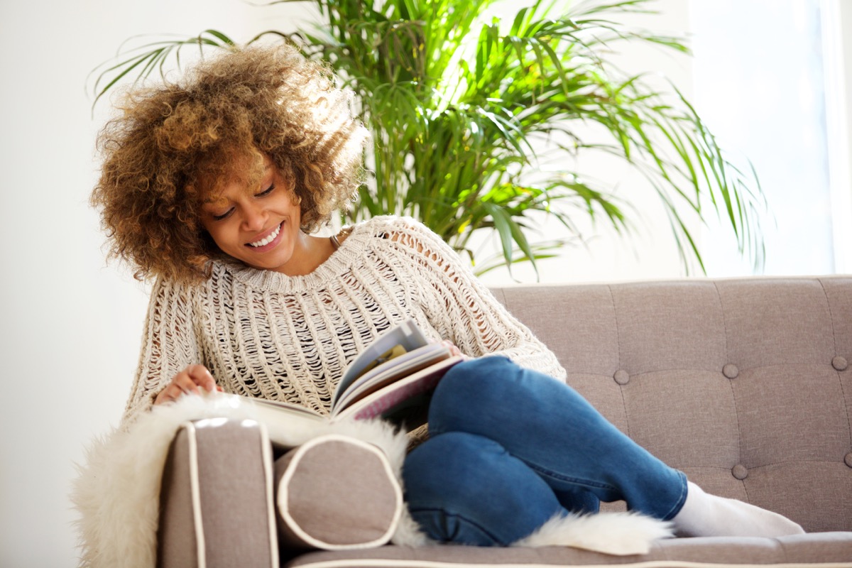 Portrait of attractive african american woman sitting on sofa reading book