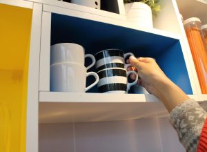 Woman's hand reaches for mug in kitchen cabinet