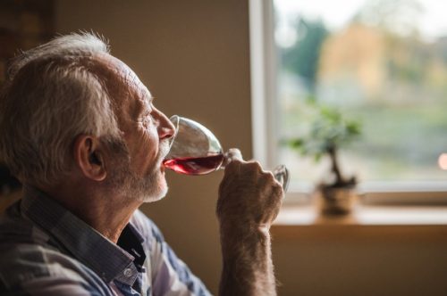 Meditierender alter Mann, der zu Hause Rotwein trinkt und wegschaut
