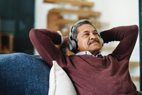 senior man of color listening to music on couch with his hands behind his head
