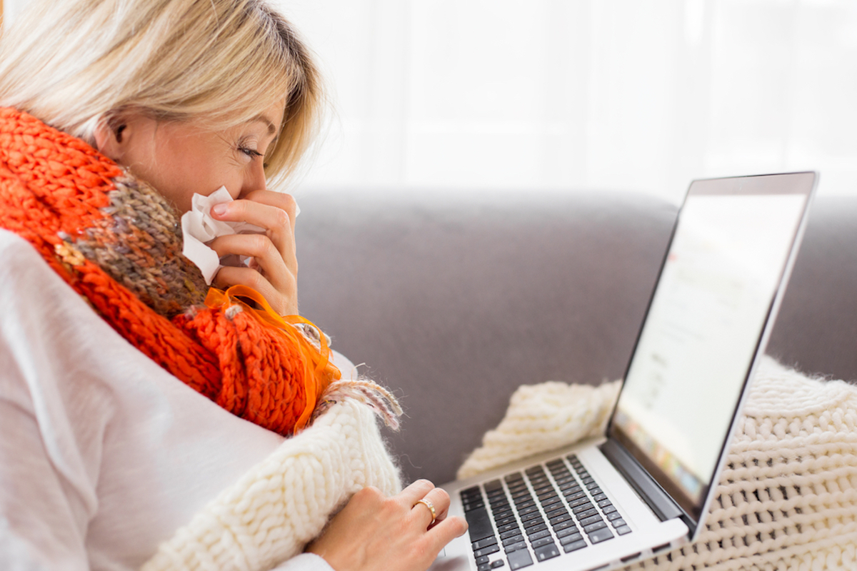 senior woman sitting on couch using laptop while blowing her nose