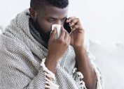 sick black man talking to doctor on phone while blowing his nowse