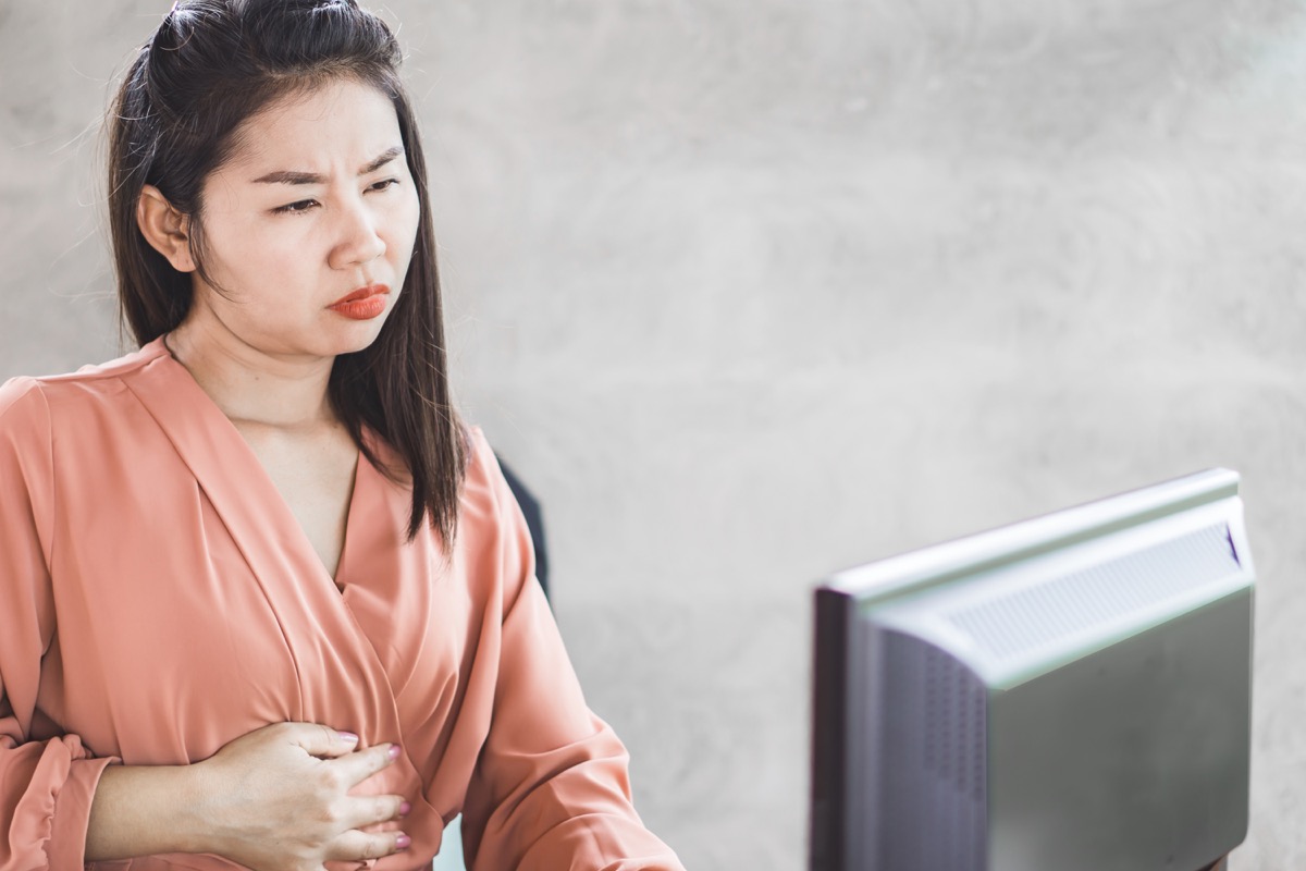 Woman experiencing stomach discomfort while working on computer