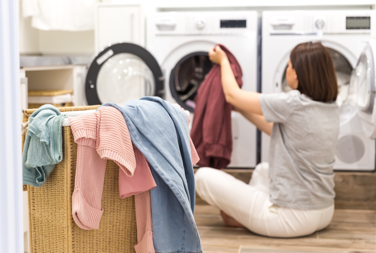 Young Woman loading washing machine and Basket Full Of Dirty Clothes In Laundry Room