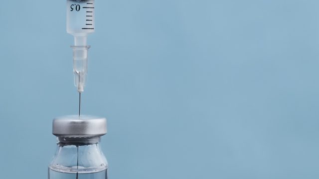 syringe dipped into vial of vaccine on blue background