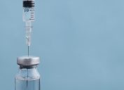 syringe dipped into vial of vaccine on blue background