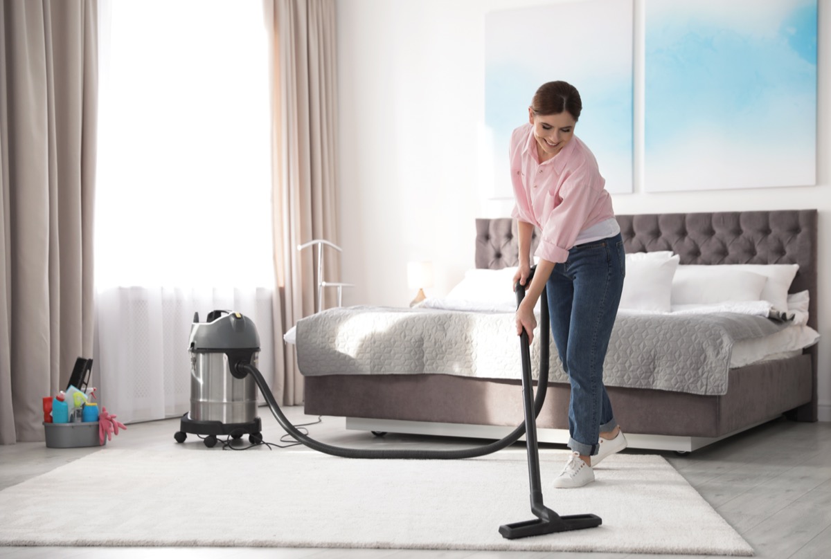 Woman vacuuming bedroom carpet