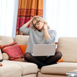 Woman with neck pain working on couch with laptop