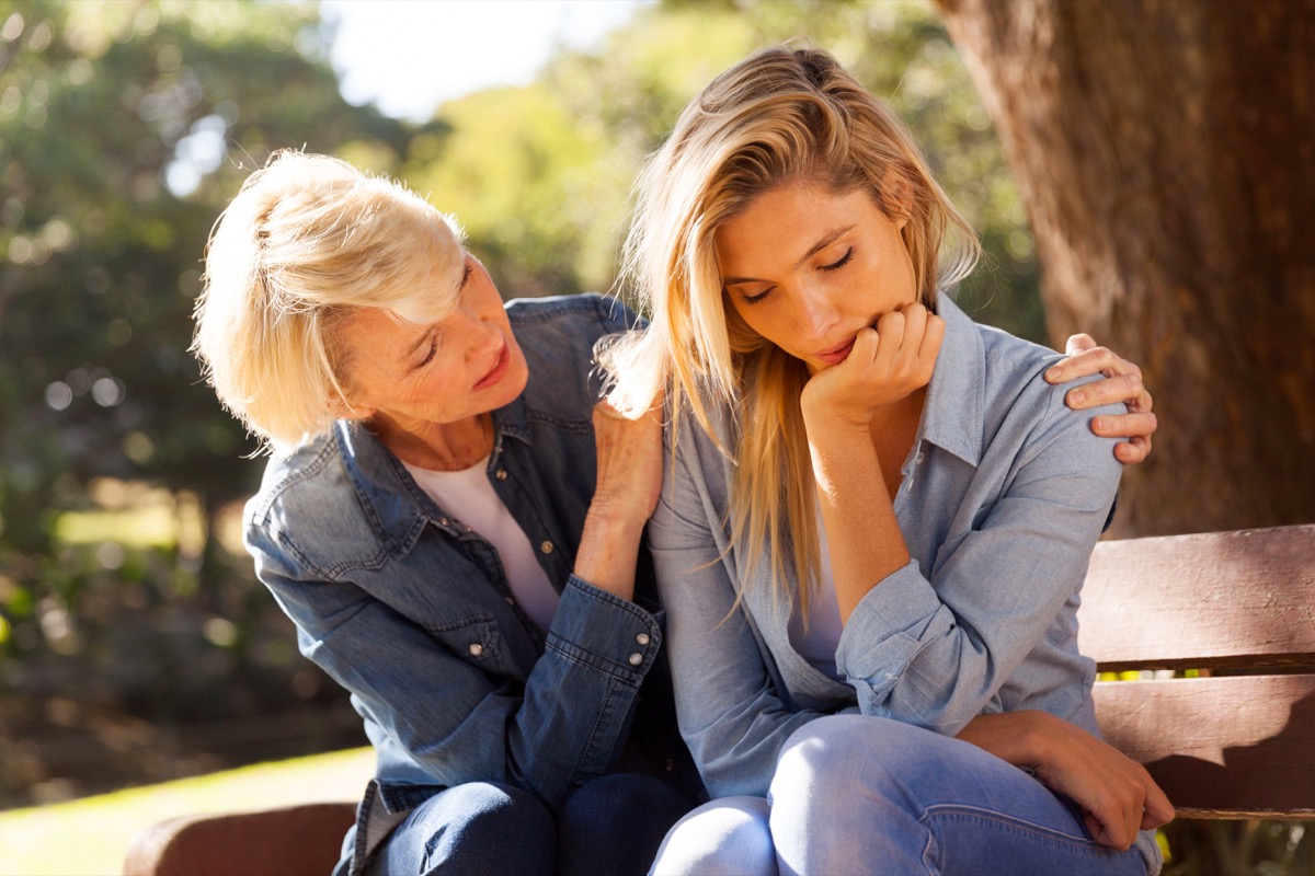 mother and daughter talking on bench outdoors; mother comforts upset-looking daughter