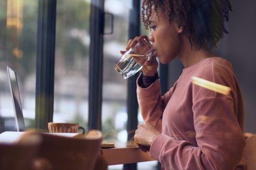black woman sitting at table on laptop drinking water