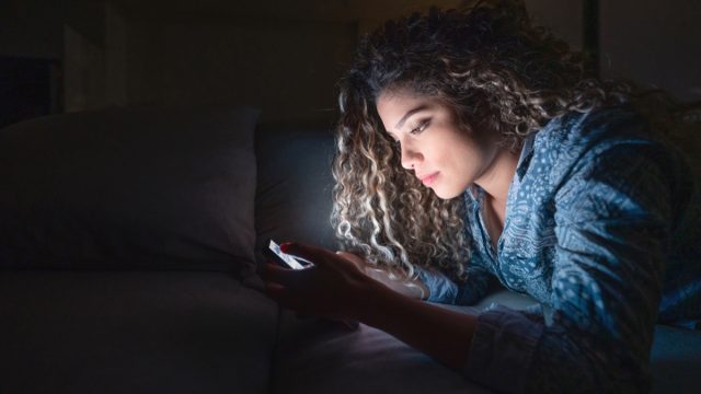Woman at home using app on her cell phone while relaxing at nighttime