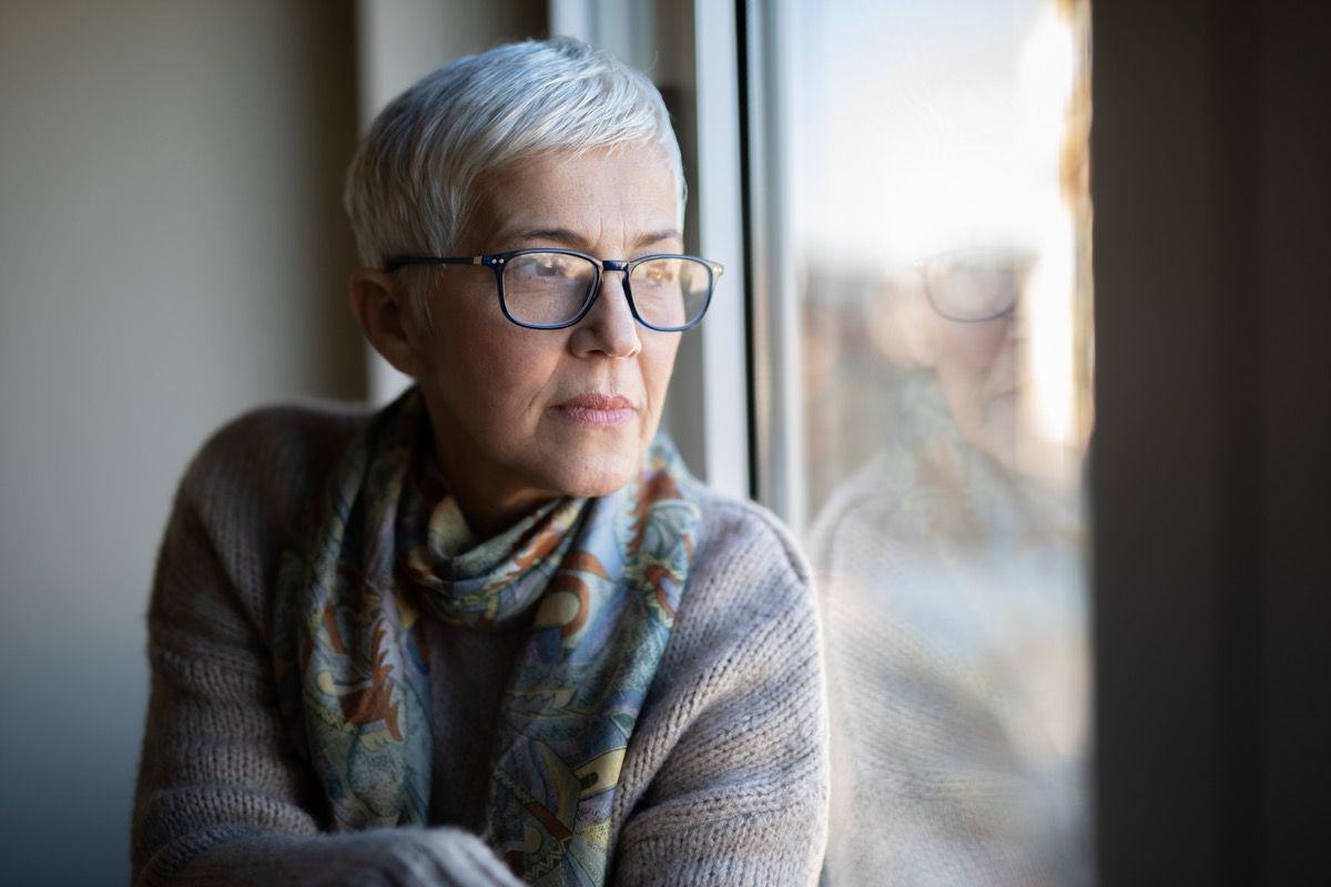 Smiling senior woman day dreaming and looking through the window during her coffee time.