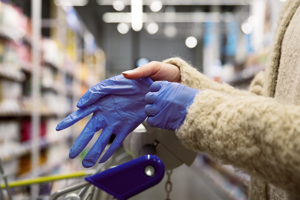 woman putting on gloves in supermarket aisle