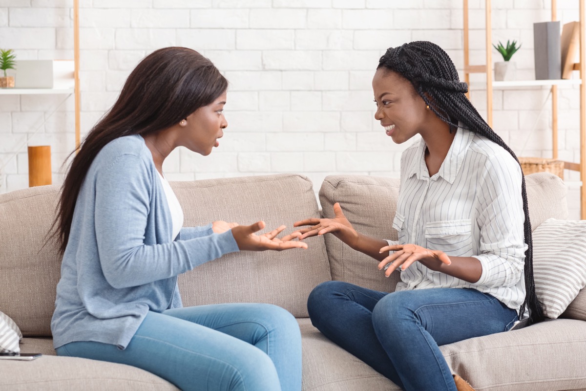 two black women sitting on a sofa and arguing with each other