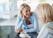 two blonde women, possibly sisters, talk at table at home over coffee