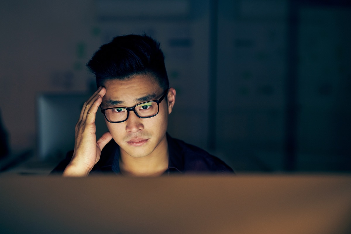 Shot of a young businessman looking stressed while using a computer at night in a modern office