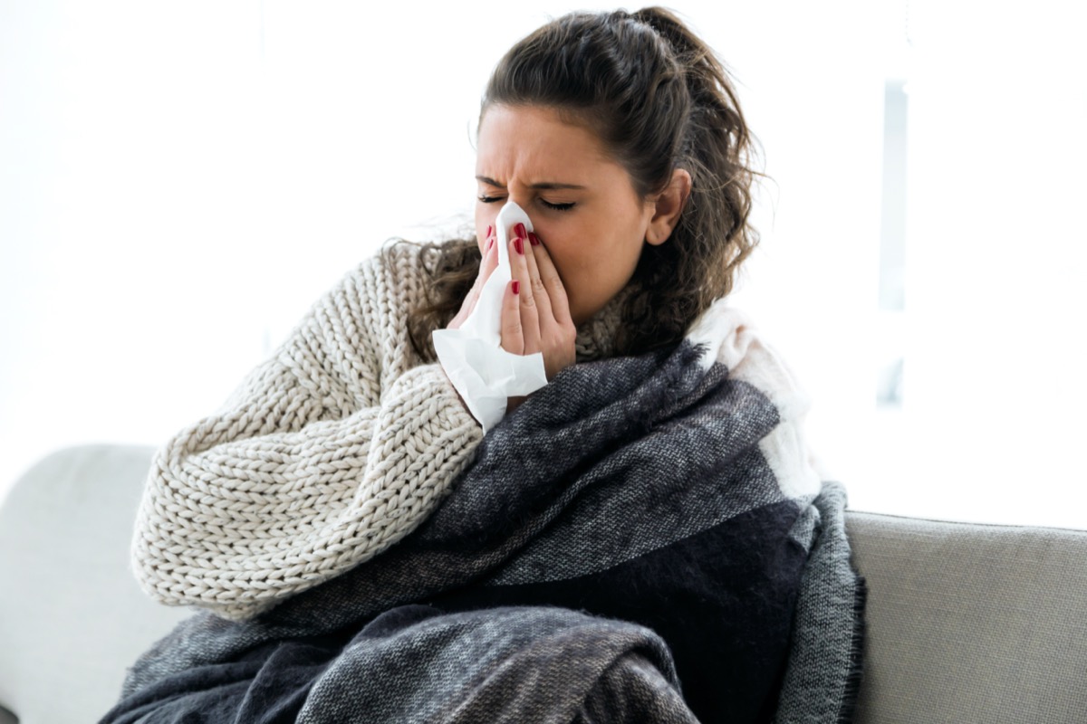 woman wrapped in blanket sneezing into tissue