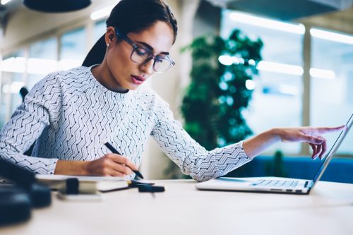 young woman writing and using computer