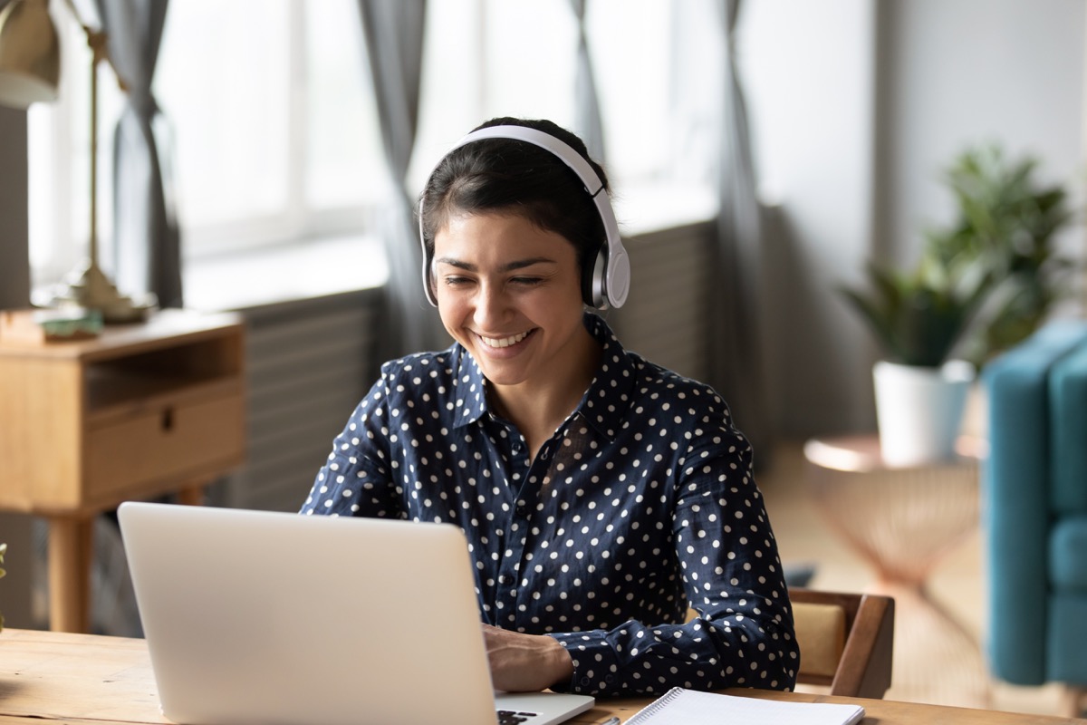 young indian woman wearing headphones in home office while working from home