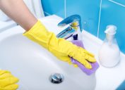 Person wearing gloves and cleaning bathroom sink