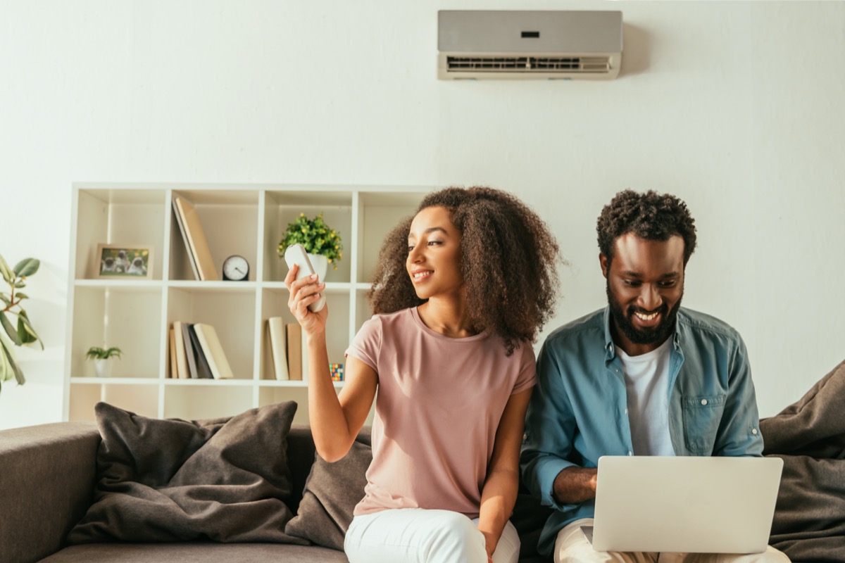 Young black couple sitting on couch and using remote-controlled air conditioner