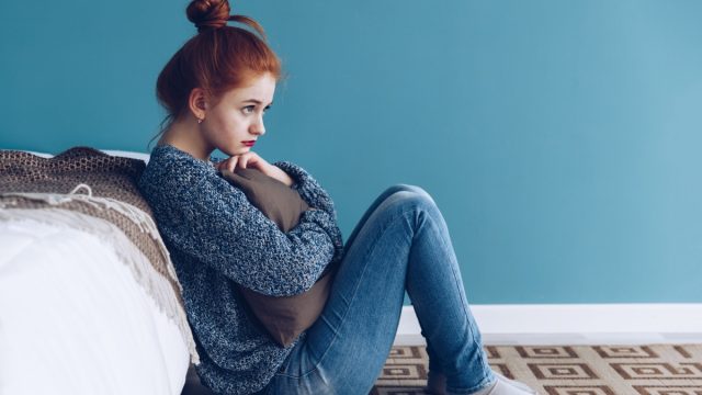 Young sad woman hugging pillow to her chest