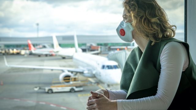 woman wearing a mask looks out the window at an airport