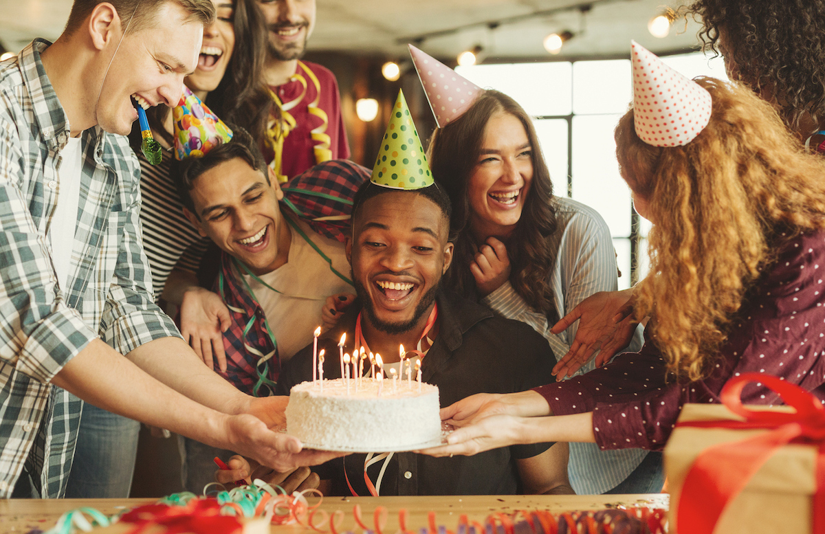 Happy black man celebrating his birthday, looking at cake with candles, surrounded by friends