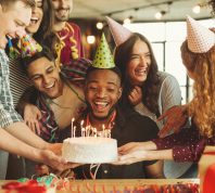 Happy black man celebrating his birthday, looking at cake with candles, surrounded by friends