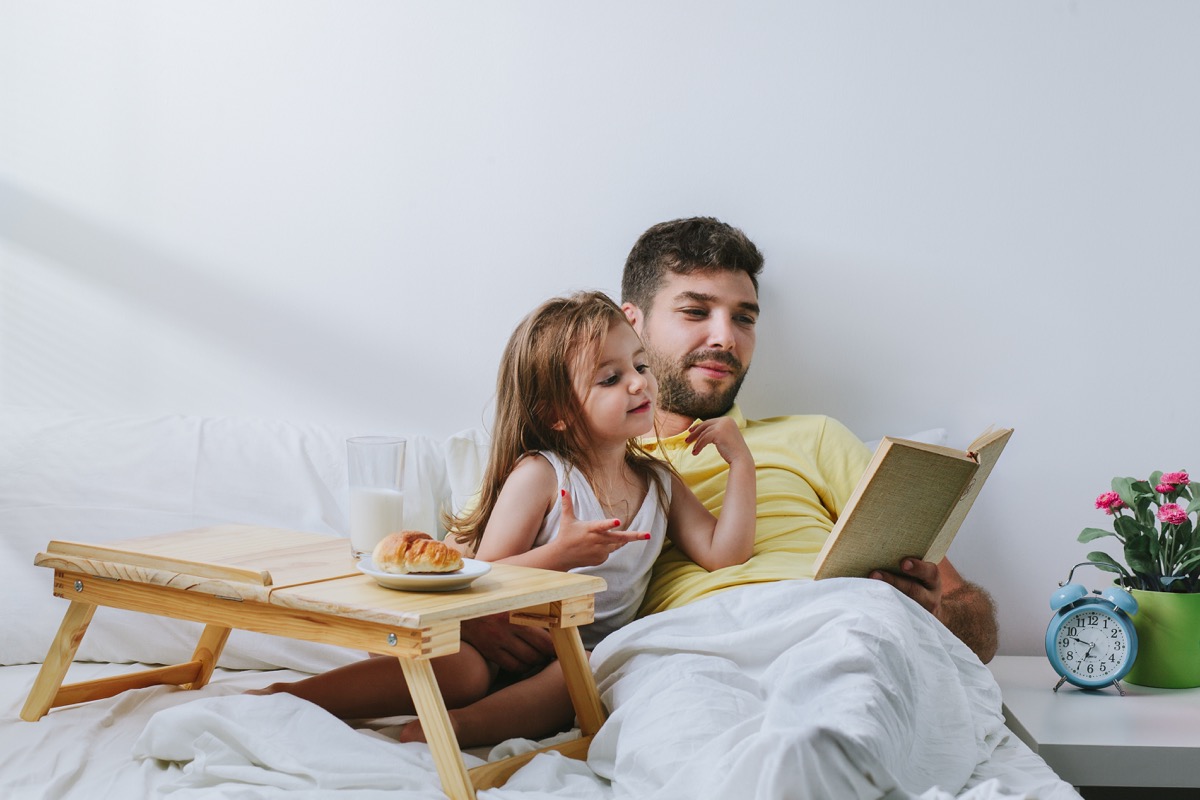 Father and daughter breakfast in bed and reading