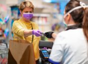 A cashier wearing gloves and a face mask hands a customer back wearing a face mask her credit card