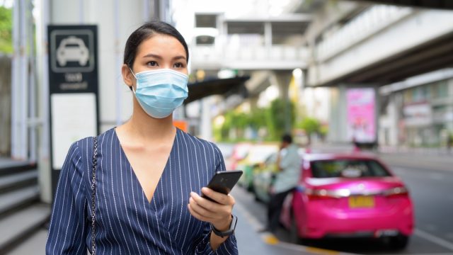 Woman in face mask holding phone in public