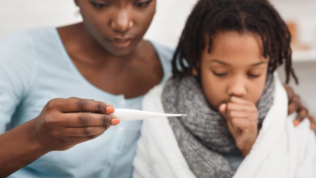 Worried black mother looking at thermometer, ill daughter coughing