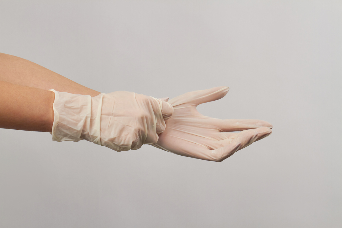 Putting on disposable sterile white gloves on white background
