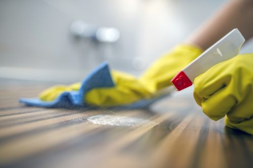 closeup of hand cleaning kitchen counter with sponge and spray disinfectant