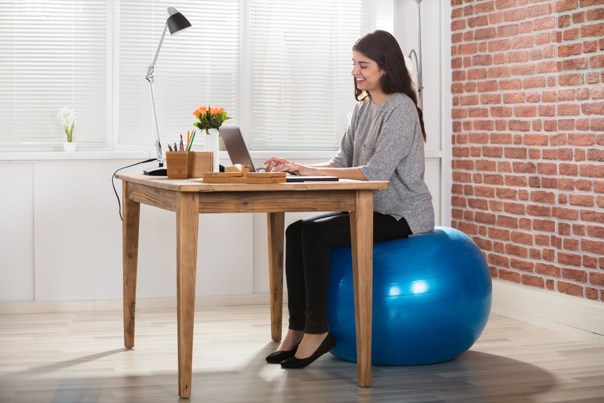 Woman using exercise ball as chair for home office desk