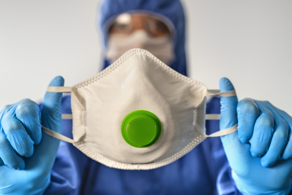 Doctor wearing highly protective suit and holding a face mask.